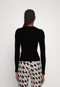 Czarny, prążkowany top z długim rękawem i okrągłym dekoltem, w zestawieniu z wzorzystymi spodniami w geometryczny wzór łańcucha w kolorze kremowym i czarnym.