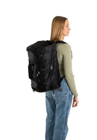 Black backpack with a textured finish, featuring bungee cord accents, side handles, and adjustable straps, worn on a person.
