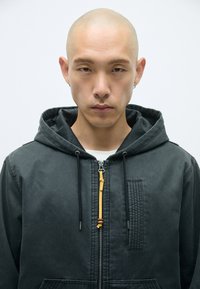 Μαύρο φούτερ μπουφάν με φερμουάρ μπροστά, με κίτρινο λεπτομέρεια στο φερμουάρ, υφασμάτινη τσέπη και κορδόνια. Λείο, ανθεκτικό ύφασμα.