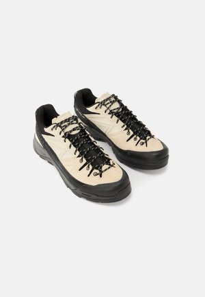 Light beige and black hiking shoes with a textured suede upper, featuring black laces and a thick rubber sole for durability.