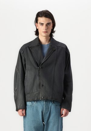 Schwarze Lederjacke mit Reverskragen, Frontreißverschluss und Knopfverschluss sowie gesteppten Details. Getragen über einem blauen T-Shirt und lockeren Jeans.
