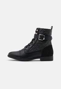 Bottines noires avec texture matelassée, avant à lacets, ceinture avec accent de boucle, et un talon bas et plat. Matériaux en suède et synthétiques.