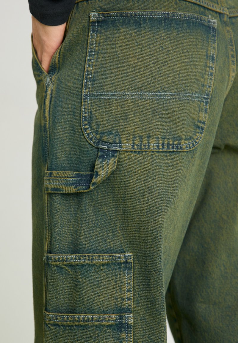 Pantaloni cargo in denim verde con più tasche, una finitura testurizzata e cuciture a contrasto, con un aspetto leggermente sbiadito.