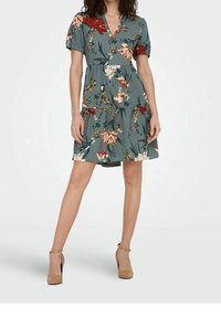 Blumenprint-Kleid in Türkis mit kurzen Ärmeln, V-Ausschnitt und mehrlagigem Rock. Es zeigt eine lebendige Mischung aus Blumen und Grünpflanzen. Das Kleid reicht bis über das Knie.