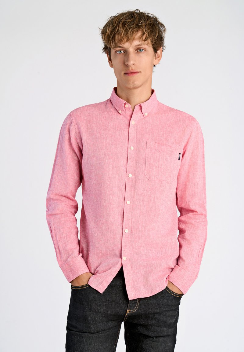 Lichtroze overhemd met knopen, gemaakt van een geweven stof met textuur, met lange mouwen en een borstzak. Draagt een donker jeans, met contrasterende stikseldetails.