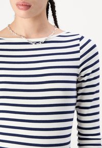 Navy and white striped long-sleeve shirt, made of soft fabric, features a boat neckline. A chunky silver chain necklace is worn on the neck.
