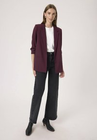 Burgundy bleiser, mille struktuursed õlad ja ühe nupuga, koos valge topi ja kõrge vöökohaga mustade laiarööpmeliste teksadega.