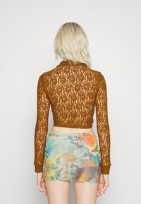 Top cropped de renda castanha com mangas longas, apresentando uma bainha recortada, combinado com uma saia mini de padrão abstrato multicolorido.