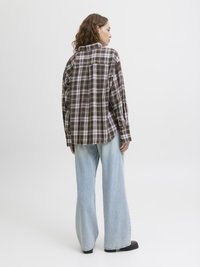 Chemise en flanelle à carreaux bruns et blancs, coupe décontractée, avec des manches longues. Associée à un jean large bleu clair et des chaussures noires.
