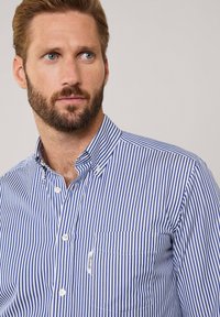 Camicia a righe blu e bianche con colletto, tasca frontale e bottoni bianchi. Tessuto fresco con linee verticali e una finitura testurizzata.