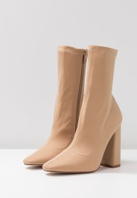 Bottines à talons hauts beiges en matière lisse, dotées d'un bout pointu et d'une fermeture éclair sur le côté intérieur. Design à talon bloc.