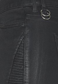 Pantalones de mezclilla negros con un panel texturizado en el lateral, acabado suave, dos aros plateados de adorno y diseño tradicional de cinco bolsillos.