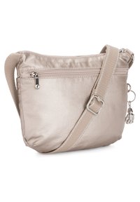 Beige crossover taske lavet af satinmateriale med en lynlåslomme, justerbar rem og en dekorativ charme. Glat tekstur, minimalistisk design.