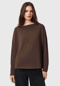 Maglietta marrone a maniche lunghe con ampio scollo a barca, vestibilità rilassata e texture morbida, abbinata a jeans scuri.