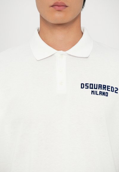 A fehér, rövid ujjú pólóing klasszikus gallérral rendelkezik, a bal oldalon kék hímzett szöveggel: „DSQUARED2 MILANO”. Texturált anyag.