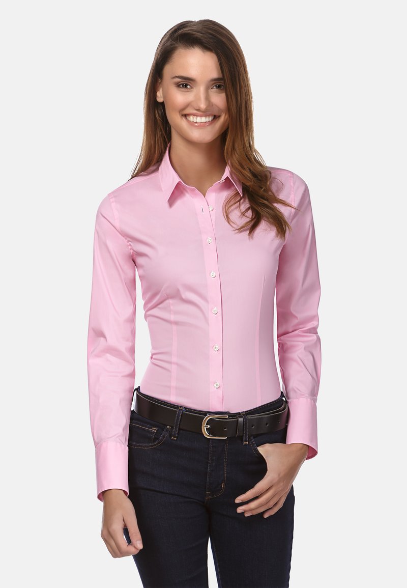 Camicia a maniche lunghe, aderente, in cotone di un rosa chiaro con colletto button-down, abbinata a jeans scuri e una cintura nera con fibbia d'argento.