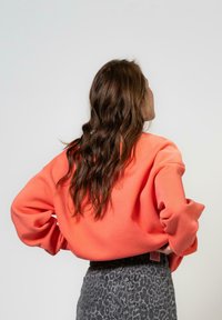 Korallkrāsas sporta krekls ar brīvu piegriezumu, pazeminātiem pleciem un ribotām rokām, apvienots ar pelēkām leoparda raksta augsto jostasvietu biksēm.