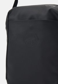 Svart tygväska med strukturerad yta, utrustad med en präglad elefantlogotyp på framsidan och en justerbar rem för bärande.