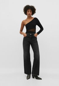 Bodysuit noir à une épaule avec panneau en maille, associé à un jean noir taille haute et à jambes larges. Des bottines noires texturées à la cheville complètent le look.
