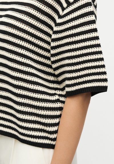 Μπλούζα με κοντά μανίκια με μαύρες και λευκές ρίγες, πλεκτή με υφή και ανοιχτό πλέγμα, που εμφανίζεται στο άνω χέρι και τον κορμό ενός ατόμου.
