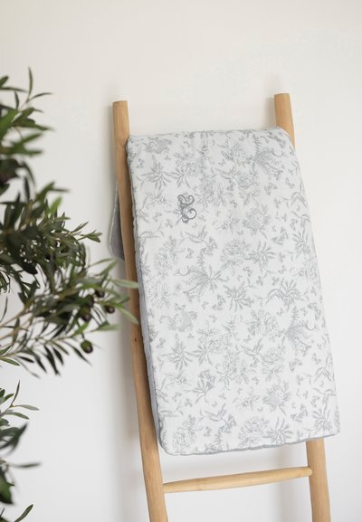 Πλεκτό κάλυμμα από γκρι και λευκό ύφασμα με λουλουδάτο μοτίβο σε ξύλινη σκάλα, που παρου σιάζει περίπλοκα βοτανικά σχέδια και μαλακή υφή.