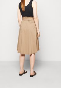 Beige A-lijn rok met een tailleband, gemaakt van lichtgewicht stof, heeft plooien en een zoom die net onder de knie valt. Draag er zwarte sandalen bij.