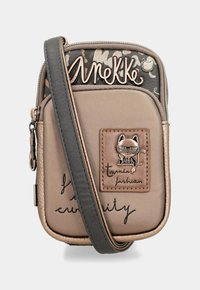 Beige Umhängetasche mit strukturiertem Vorderteil, ausgestattet mit einer katzenförmigen Hardware-Akzentuierung, metallic Logo und handschriftlichem Text. Verstellbarer Schulterriemen inklusive.