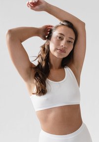 Weißer Baumwoll-Sport-BH mit Rundhalsausschnitt, elastischem Band und nahtlosem Design. Hautfarbe im natürlichen Licht sichtbar.