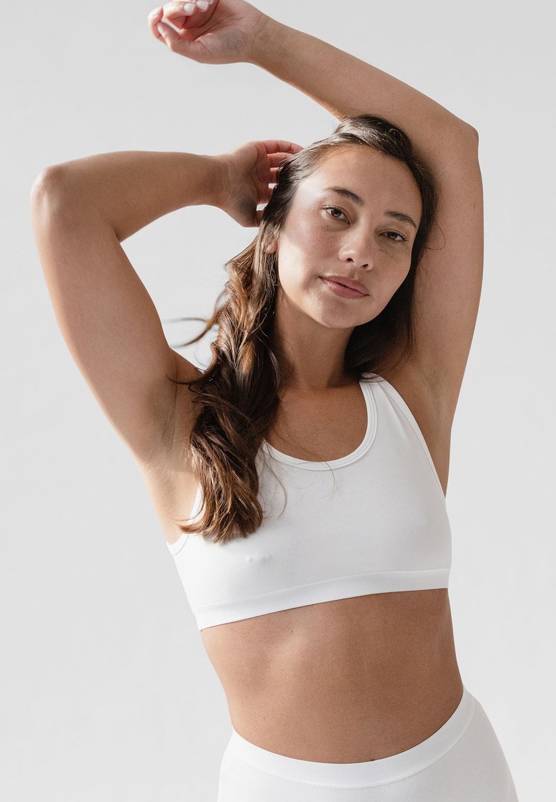 Weißer Baumwoll-Sport-BH mit Rundhalsausschnitt, elastischem Band und nahtlosem Design. Hautfarbe im natürlichen Licht sichtbar.
