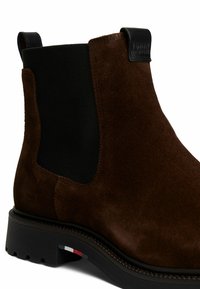 Stivaletto in nabuk marrone con pannelli laterali elastici, linguetta in pelle nera e suola in gomma testurizzata con un accento tricolore vicino al tallone.