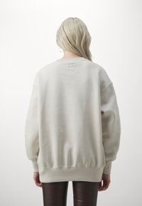 Light beige sweatshirt with oversized silhouette, ribbed cuffs and hem, and a small Nike logo tag on the back. Texture appears soft.