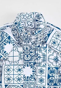 Veste en duvet avec un motif de carreaux géométriques bleus et blancs. Le matériau a l'air brillant, avec un col haut et une fermeture à boutons.