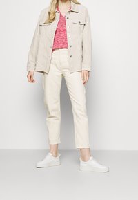 Beige corduroy jasje over een roze gebreid shirt, gecombineerd met crèmekleurige tapered broek en witte sneakers. Materialen en kleuren zijn eenvoudig en licht.