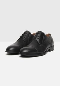 Schwarze Leder-Halbschuhe mit glatter Oberfläche, abgerundetem Zehenbereich und dezentem Stickdetail über dem Obermaterial. Schnürdesign mit niedrigem Absatz.