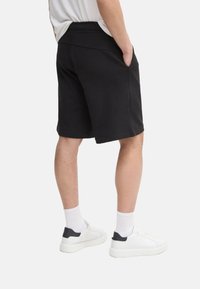 Pantalones cortos deportivos negros con una textura suave, diseño de largo hasta la rodilla, bolsillos laterales y una cómoda cinturilla elástica, combinados con zapatillas blancas.