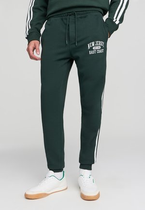 Pantaloni jogger di colore verde scuro realizzati in misto cotone, con toppe laterali bianche, vita con coulisse e stampa "NEW JERSEY EAST COAST".