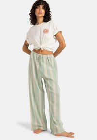 Witte top met korte mouwen en een geknoopte voorkant. Lichtgroene en beige gestreepte broek met wijde pijpen en een elastische tailleband.