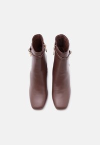 Καφέ δερμάτινα μποτάκια αστραγάλου με πλαϊνά φερμουάρ και διακοσμητικά λουριά, απεικονισμένα από πάνω σε λευκό φόντο.