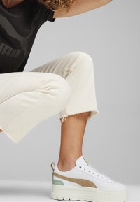 Vita sneakers med tjock sula, beige och mintaccents, och texturerade detaljer. Bärs tillsammans med ljusa, korta, fransiga byxor.