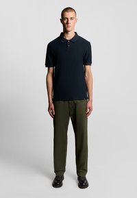 Marineblå polo-shirt med ribbet krave og korte ærmer, parret med olivengrønne lige bukser og sorte sko. Enkelt design overordnet.