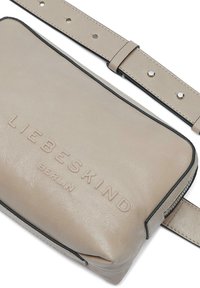 Borsa a tracolla in pelle beige con finitura testurizzata, logo impresso e bordi neri. Include una tracolla regolabile abbinata con accessori metallici.