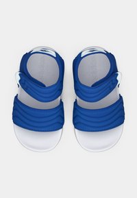 Μπλε σανδάλια με κυματιστούς υφασμένους ιμάντες, κλεισίματα με βέλκρο και λευκή σόλα. Κατασκευασμένα από ελαφρύ υλικό, σχεδιασμένα για άνεση και ευκαμψία.