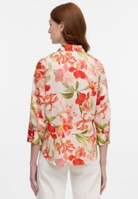 Floral shirt in light fabric featuring red and green flowers on a beige background. Three-quarter sleeves with button details at cuffs.
