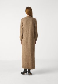 Long brown knit dress with long sleeves, a crew neck, and side slits at the hem. Worn with black ankle boots and smooth, soft texture.