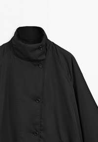 Black high-collared coat with asymmetrical button closure and long sleeves against a plain light background.
