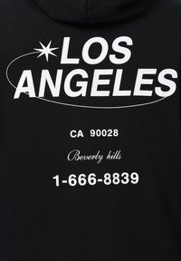 Sudadera negra con texto blanco que muestra "LOS ÁNGELES", "CA 90028", "Beverly hills" y un número de teléfono. Textura de tela de algodón suave.