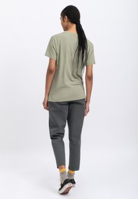 Olijfgroen t-shirt met korte mouwen in combinatie met grijze tapering broek, voorzien van een eenvoudig ontwerp, zichtbare stoftextuur en casual schoeisel.