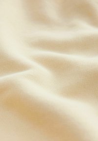 Tessuto di cotone beige con una superficie liscia e un sottile motivo a coste. Il materiale cade dolcemente, creando pieghe e onde delicate.
