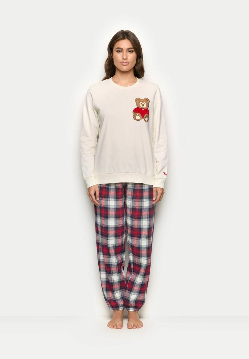 Kremowa bluzka z długim rękawem z motywem misia na piersi oraz czerwone spodnie piżamowe w kratę z elastycznymi mankietami. Miękki, casualowy materiał.