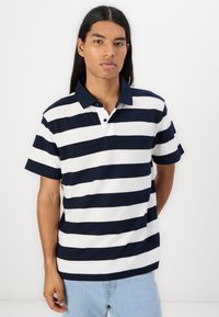 Polo de manga curta em riscas azul marinho e brancas, com colarinho azul marinho sólido, listel de botões e um tecido texturizado.